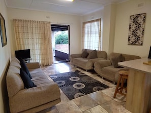 A living room with a sofa, a coffee table, and a TV. There is a door leading to an outdoor area. - Klein Paradys (Port Shepstone)
