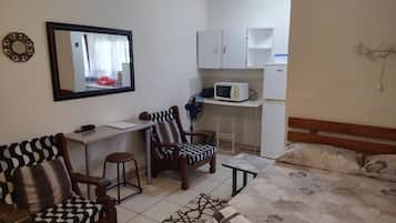 A compact room with a bed, a desk, a chair, a microwave, and a mirror.
