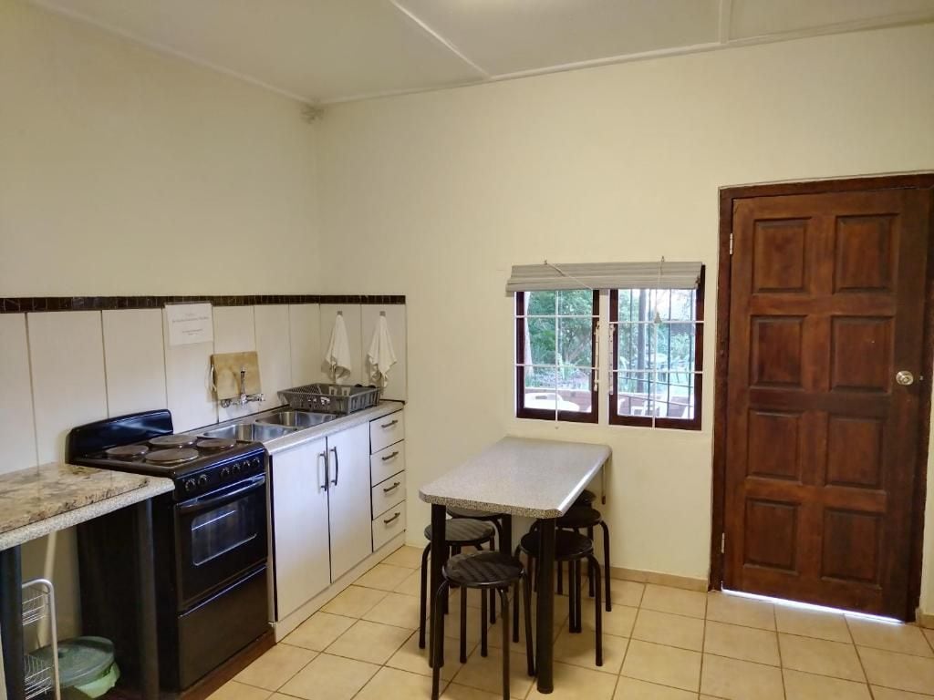 A kitchen with a stove, sink, and a window with a view. There is a wooden door and a table with chairs.