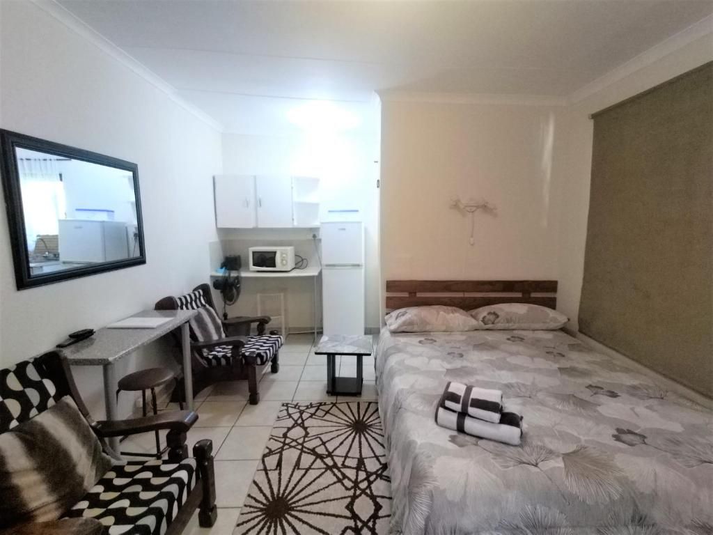 Een kleine hotelkamer met een bed, een bureau, een stoel, een tafeltje en een magnetron.