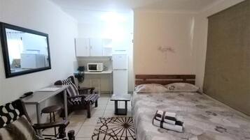Een kleine hotelkamer met een bed, een bureau, een stoel, een tafeltje en een magnetron.