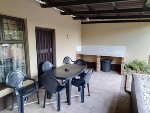 An outdoor patio with a table and chairs, a brick fireplace, and a covered area with a roof. - Klein Paradys (Port Shepstone)