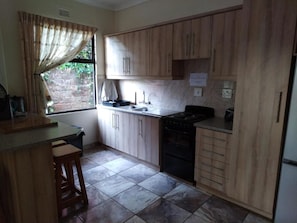 A kitchen with wooden cabinets, a stove, and a sink. - Klein Paradys (Port Shepstone)
