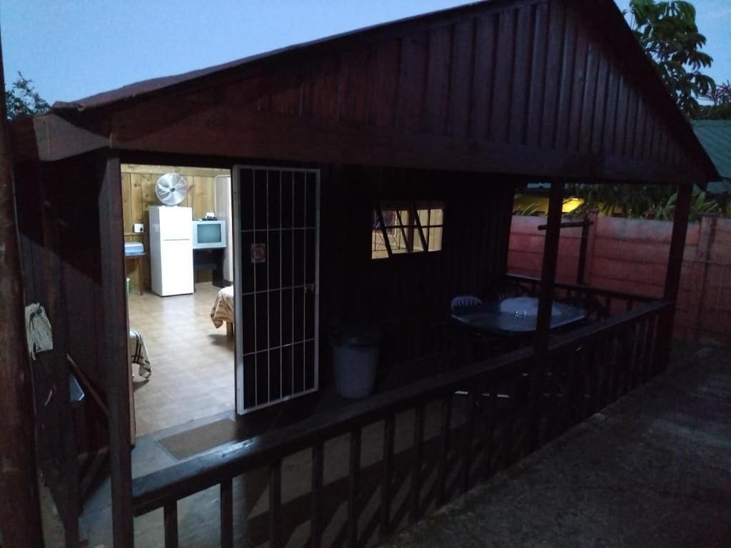 Una construcció de fusta amb una zona exterior coberta, taula de dinar i cuina visible a l'interior.