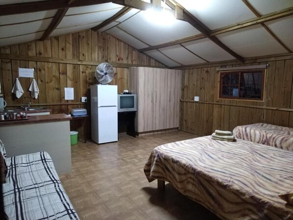 A room with a bed, a small kitchenette, a fan, and wooden walls. - Klein Paradys (Port Shepstone)