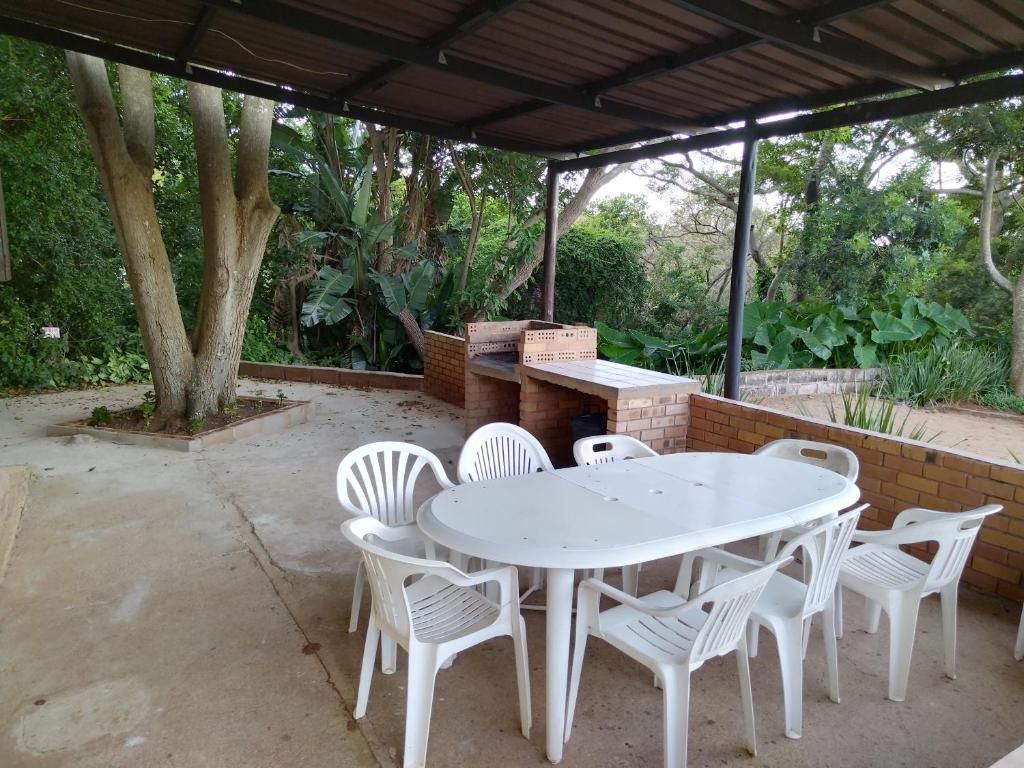 An outdoor patio with a round table and white plastic chairs, surrounded by a brick wall and covered by a metal roof.