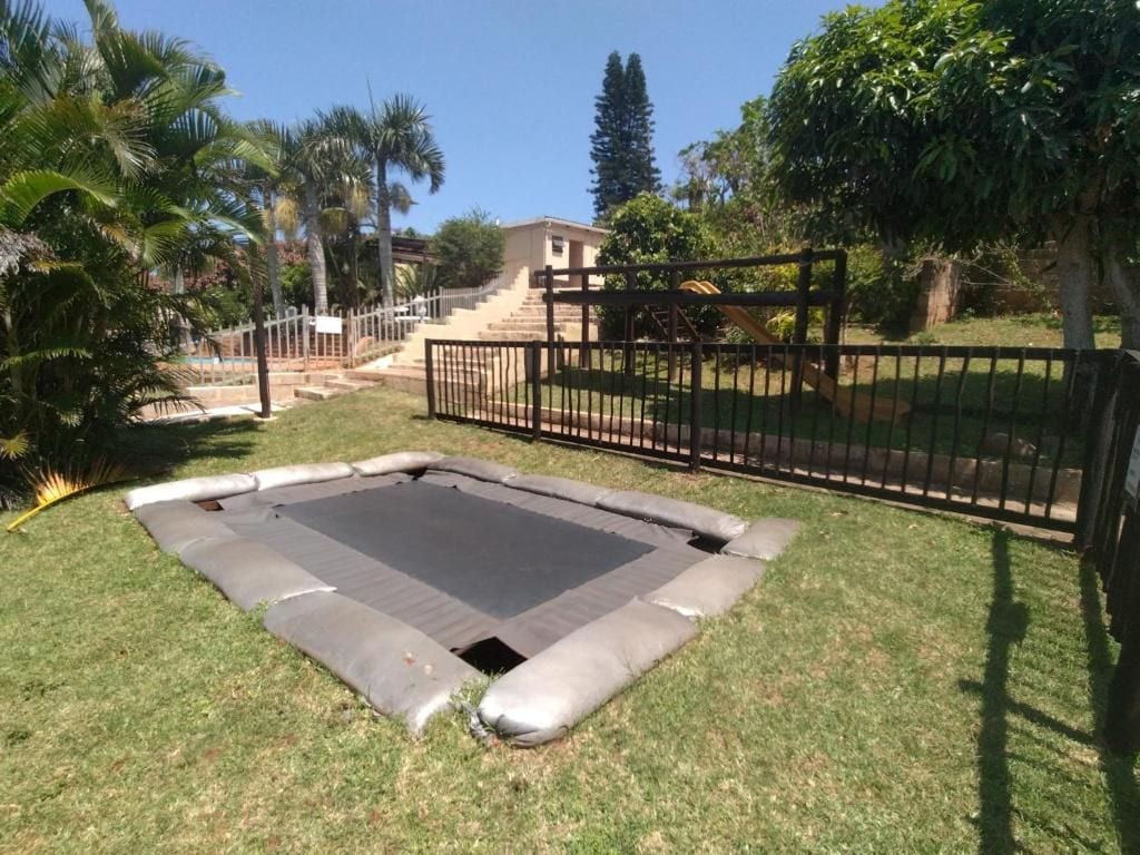 Ein Trampolin in einem Rasen mit einem Zaun und Treppen, die zu einem Gebäude führen.