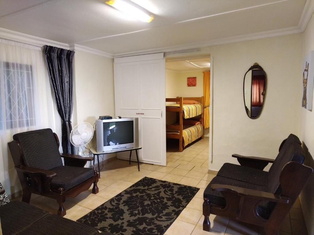 Una sala de estar con televisor, dos sillones, un sofá, un ventilador y un armario.