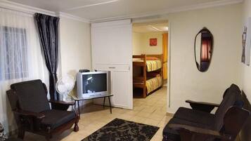 Una sala de estar con televisor, dos sillones, un sofá, un ventilador y un armario.