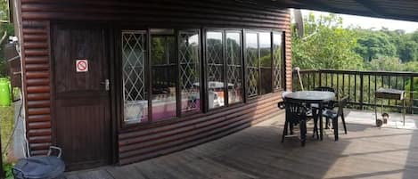 A wooden deck with a table and chairs, a covered area with a railing, and a door with a window.