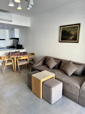 Un salon moderne avec un canapé gris, une table basse en bois et un coin repas comprenant une table et des chaises.