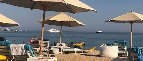 Une plage avec des parasols, des chaises longues et une étendue de sable.