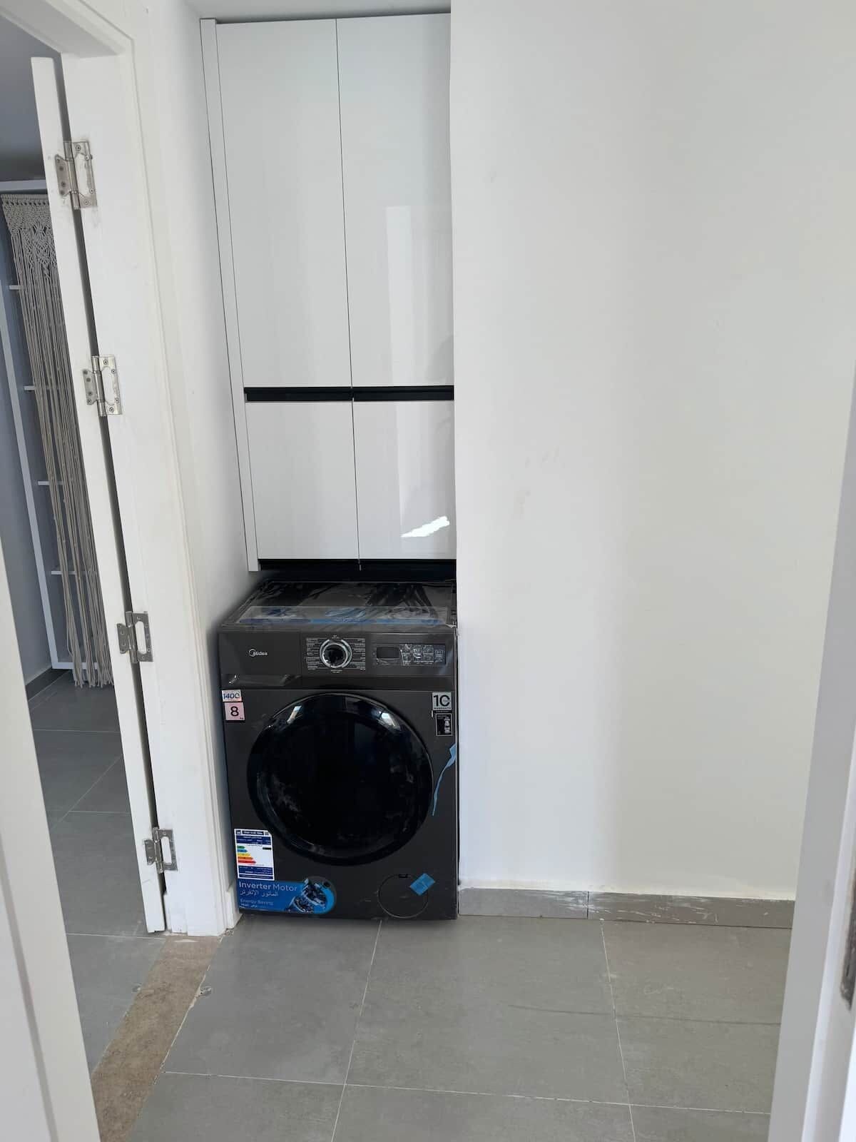 Une petite buanderie équipée d’un lave-linge et d’un meuble blanc.