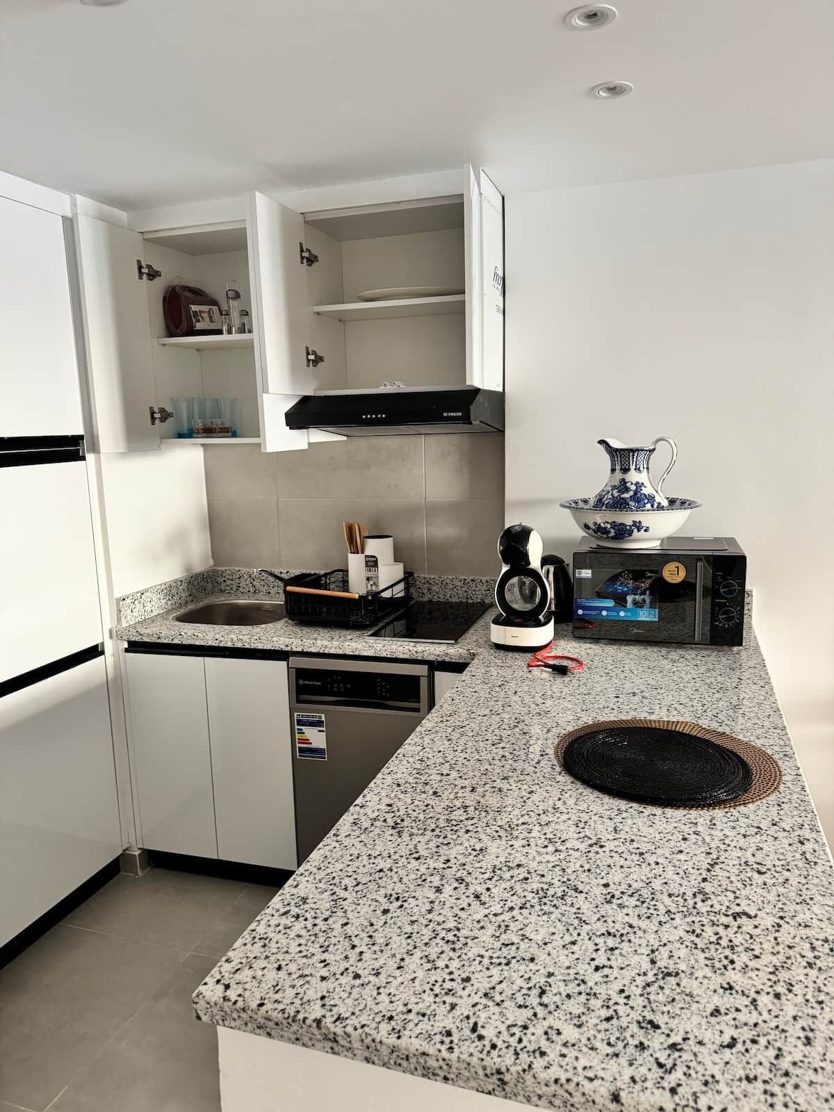 A compact kitchen with white cabinetry, a granite countertop, a dishwasher, a coffee maker, and a microwave.