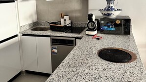 Uma cozinha compacta com armários brancos, bancada de granito, lava-louças, cafeteira e micro-ondas.