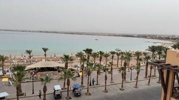 Blick auf einen Strand mit Palmen, einer überdachten Sitzgelegenheit und Meer.