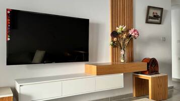 Ein modernes Wohnzimmer mit einem Flachbildfernseher an einer weißen Konsole, einer Holz-Akzentwand, einer Vase mit Blumen und einem kleinen Holztisch.
