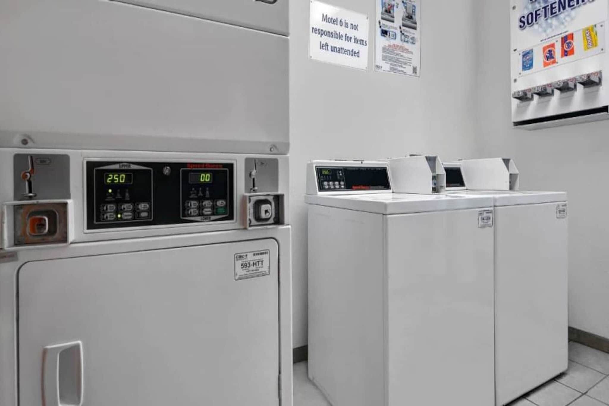 A laundry room with two washing machines, a control panel, and a sign indicating the motel's policy on unattended items.