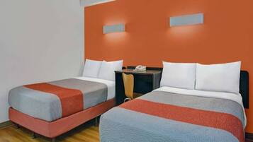Ein Hotelzimmer mit zwei Betten, jedes mit einer grau-roten Decke, weißen Kissen und einem kleinen Tisch mit einem Telefon.