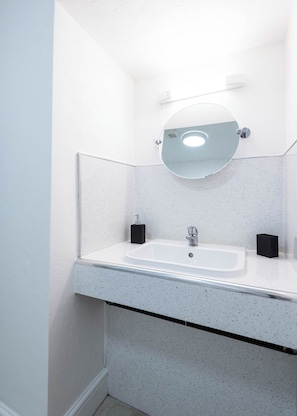 A bathroom with a white sink, a round mirror, and two black soap dispensers. - The Stanley Arms Hotel by Guestz (Seascale)
