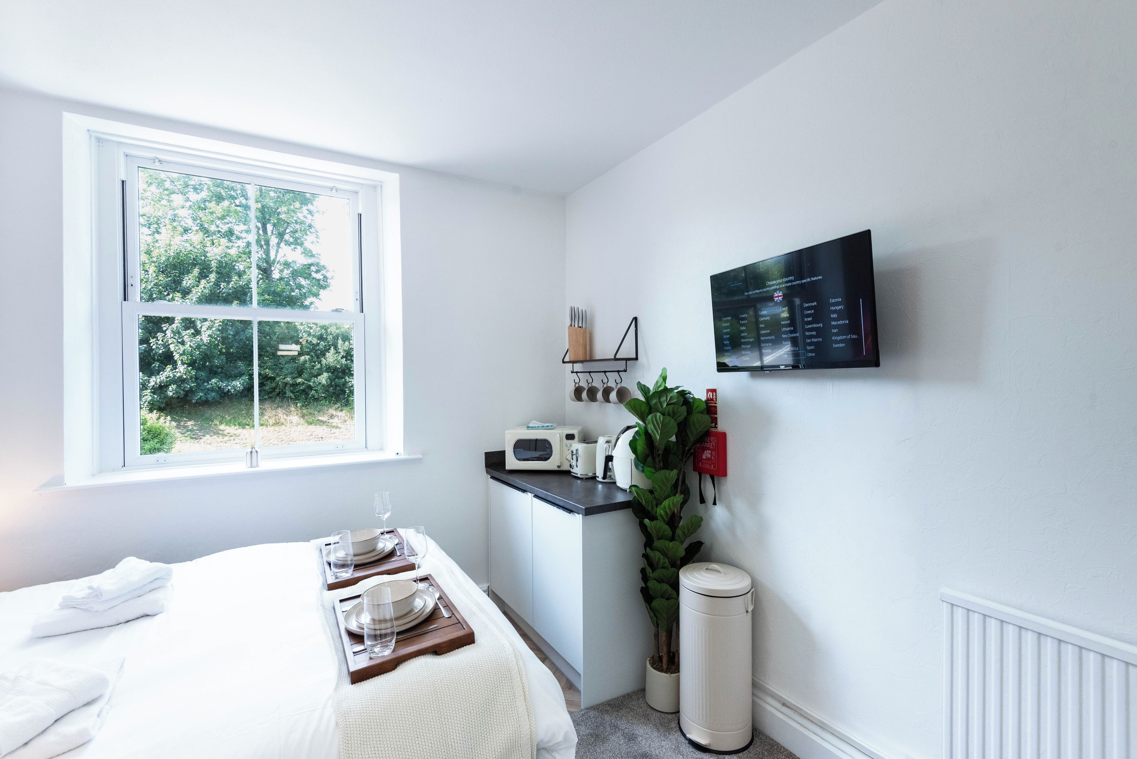 A hotel room with a bed, a breakfast bar, a TV, and a window with a view of trees.