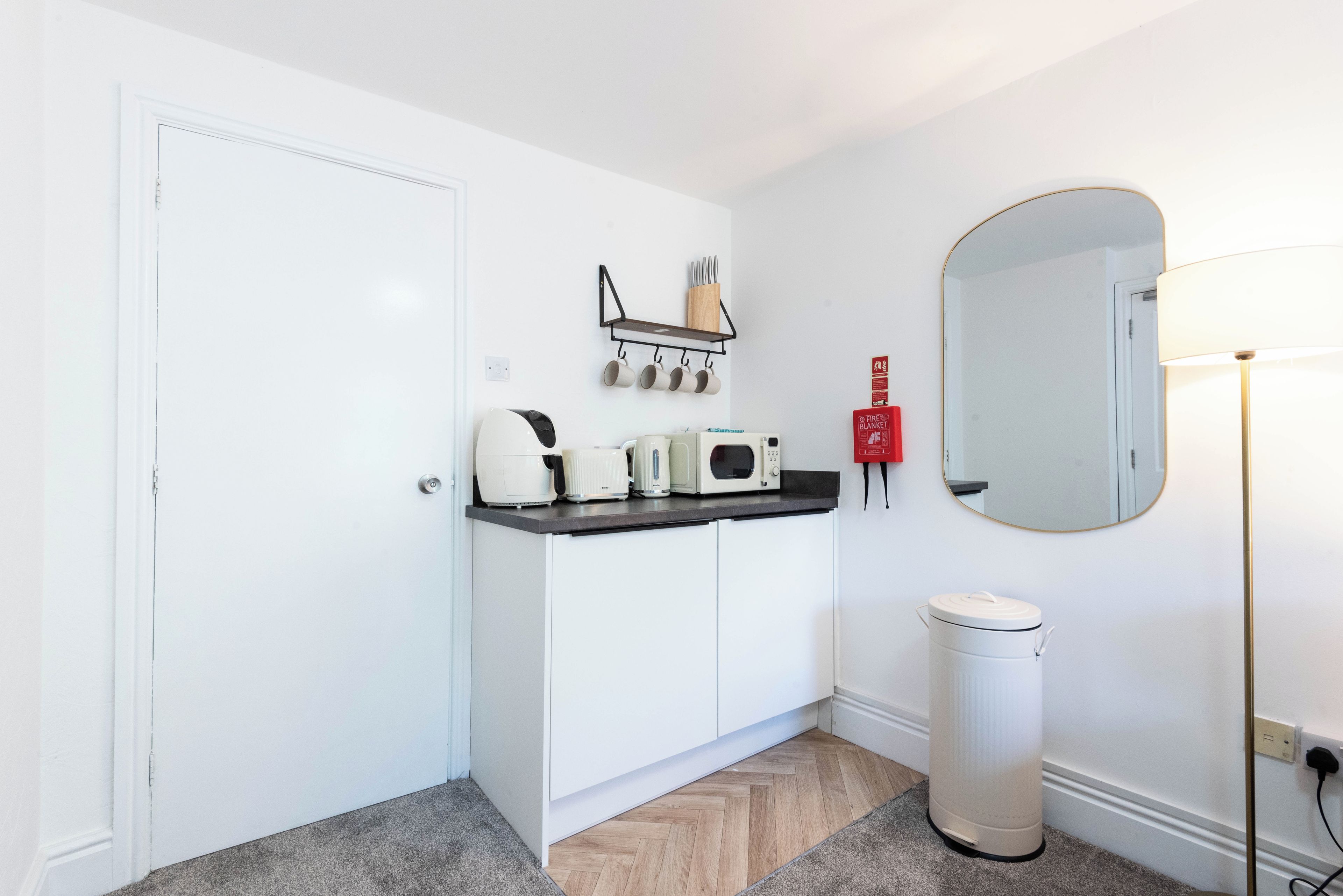 A white door, a kitchen counter with a coffee maker, a microwave, and a trash can.