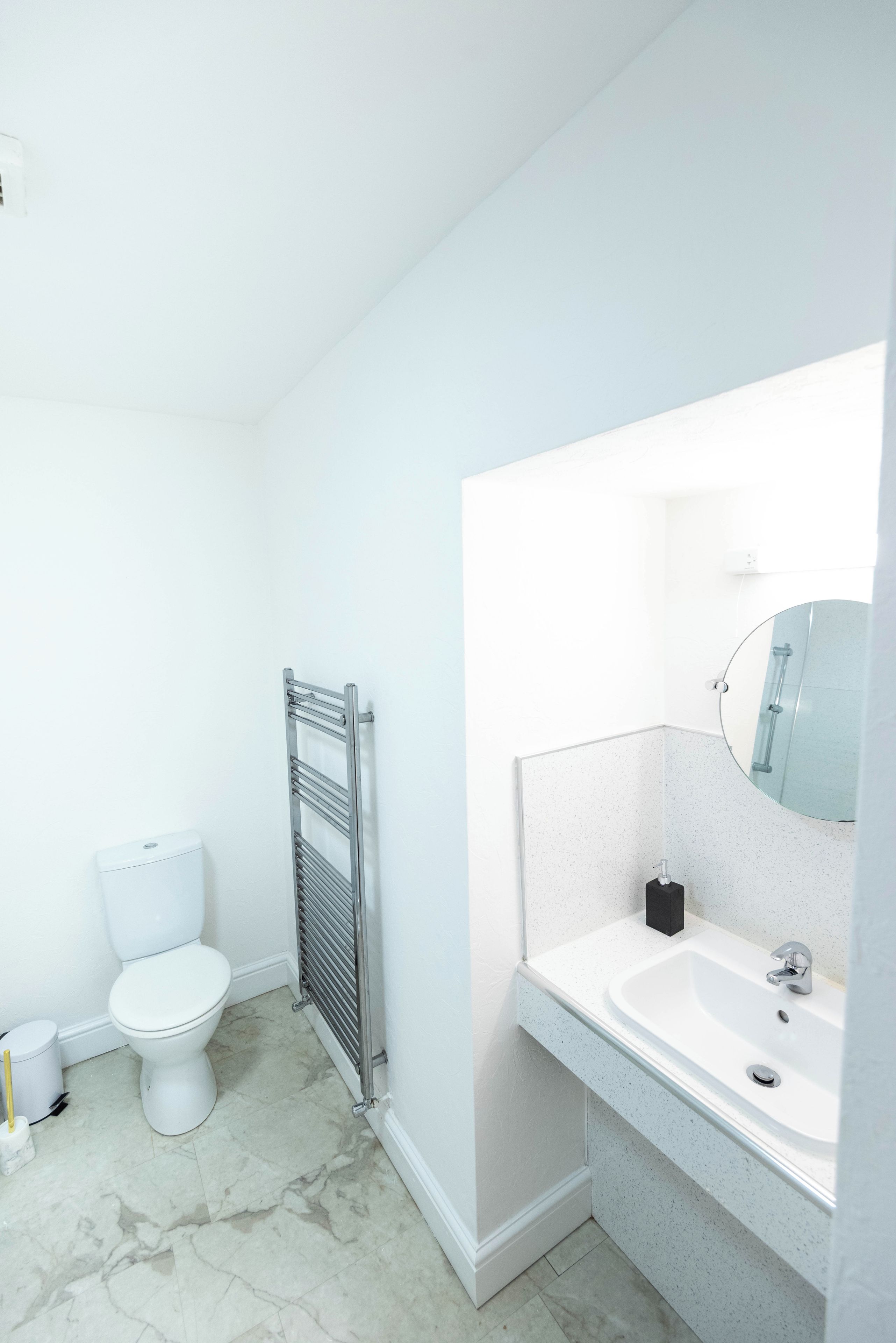 A bathroom with a toilet, a towel rack, a sink with a mirror, and a shower area.