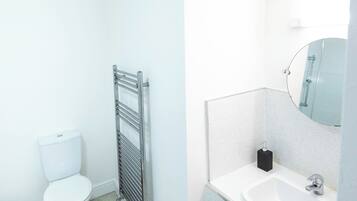A bathroom with a toilet, a towel rack, a sink with a mirror, and a shower area.