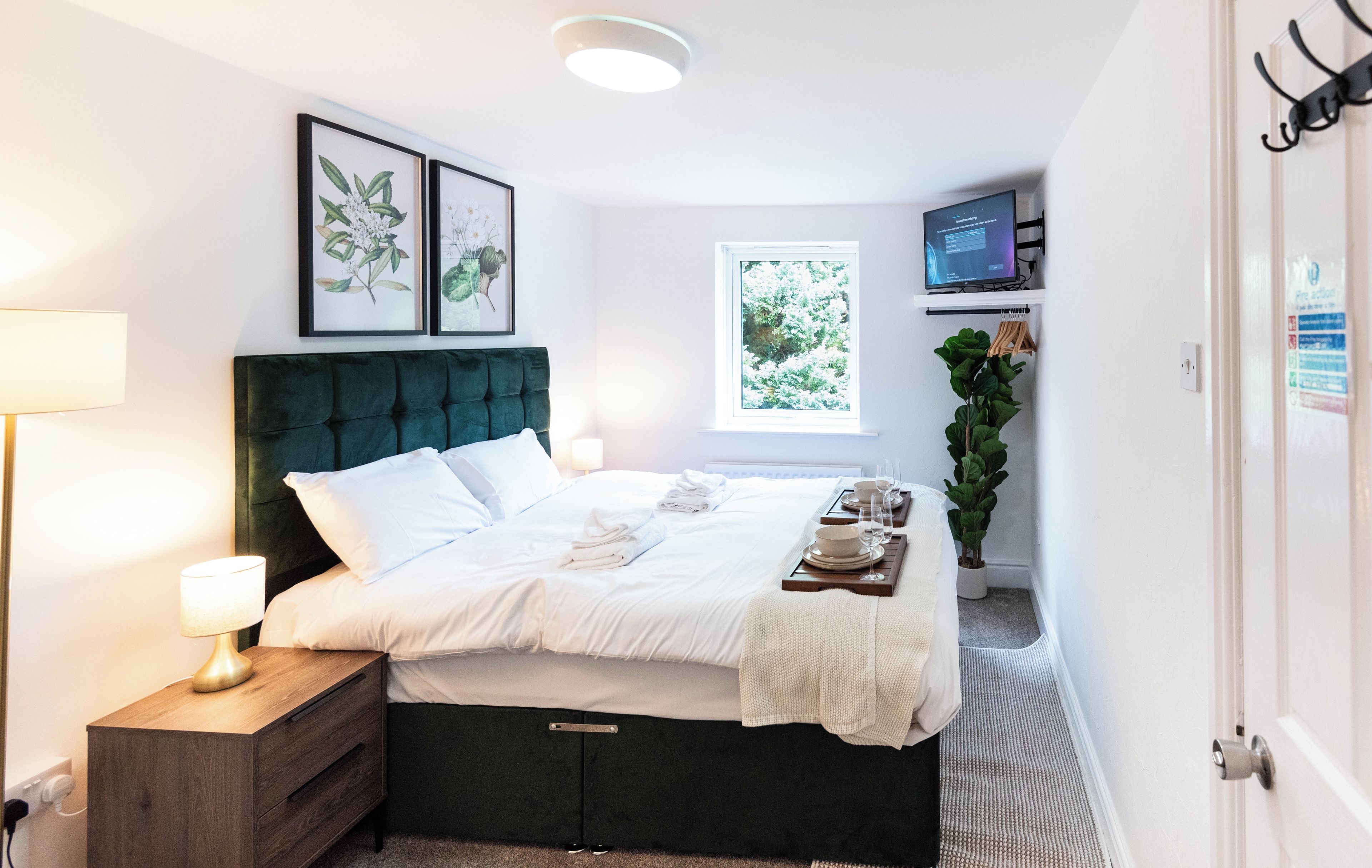 A neatly made bed with white linens, a bedside lamp, and a small wooden nightstand.