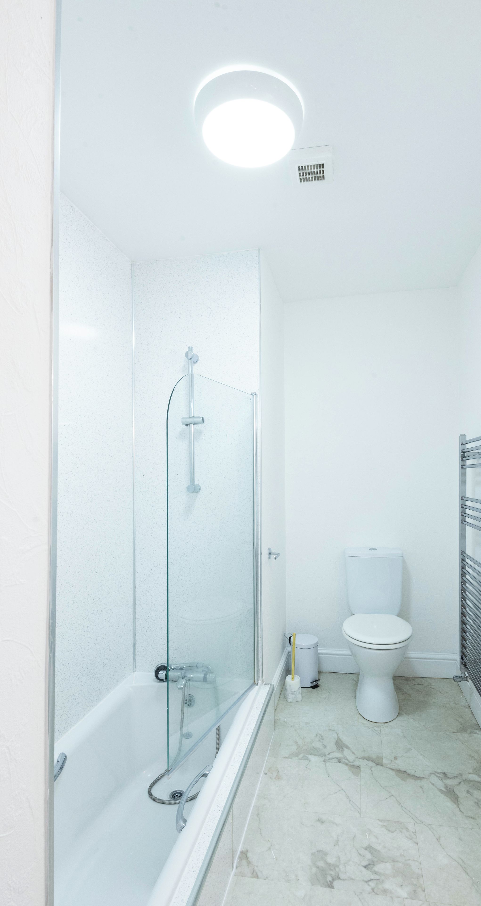 A modern bathroom with a glass-enclosed shower, a white toilet, and a marble floor.