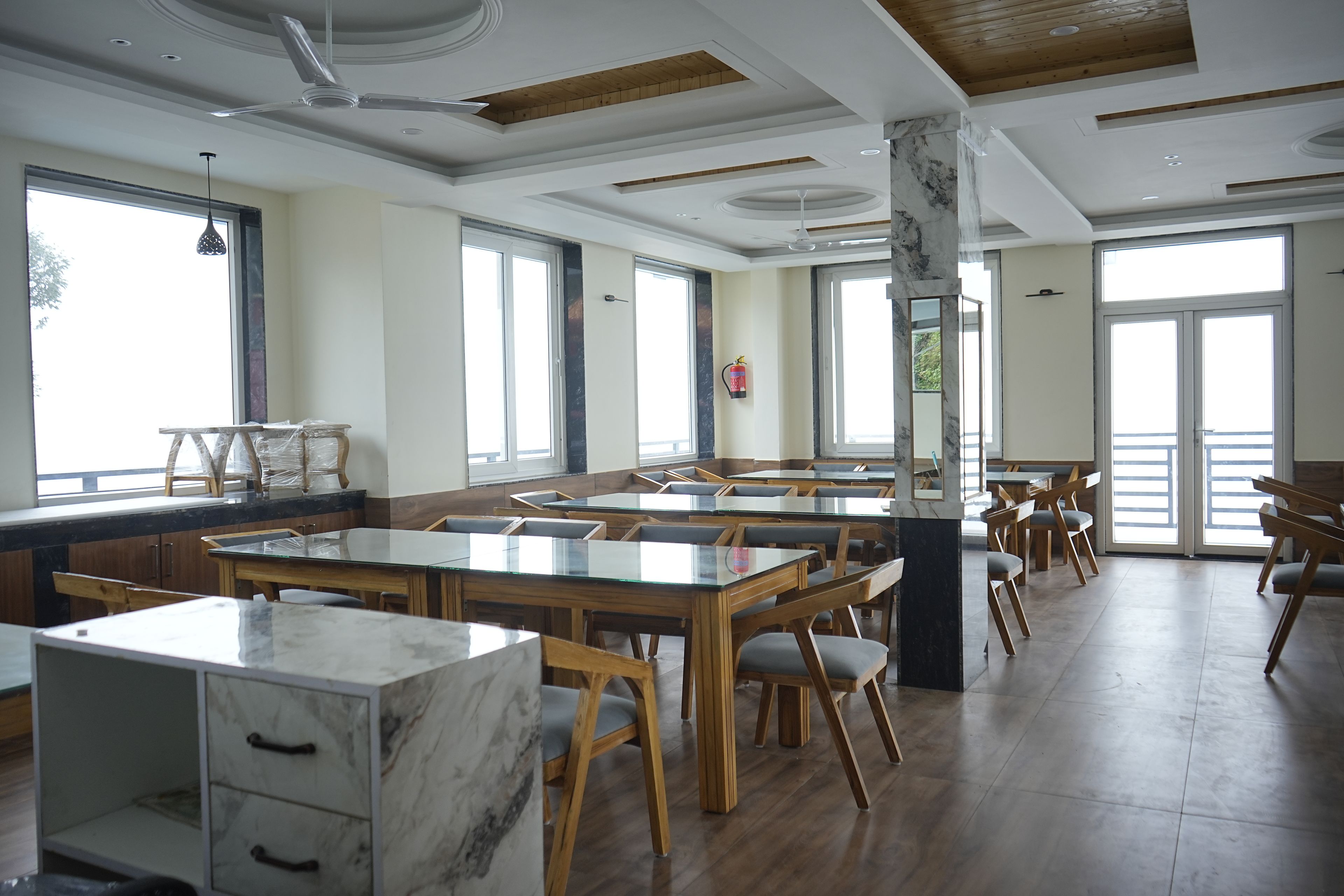 Uma ampla sala de jantar com várias mesas e cadeiras, janelas grandes e um design moderno no teto.