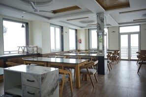 Un comedor amplio con varias mesas y sillas, ventanas grandes y un diseño moderno de techo.