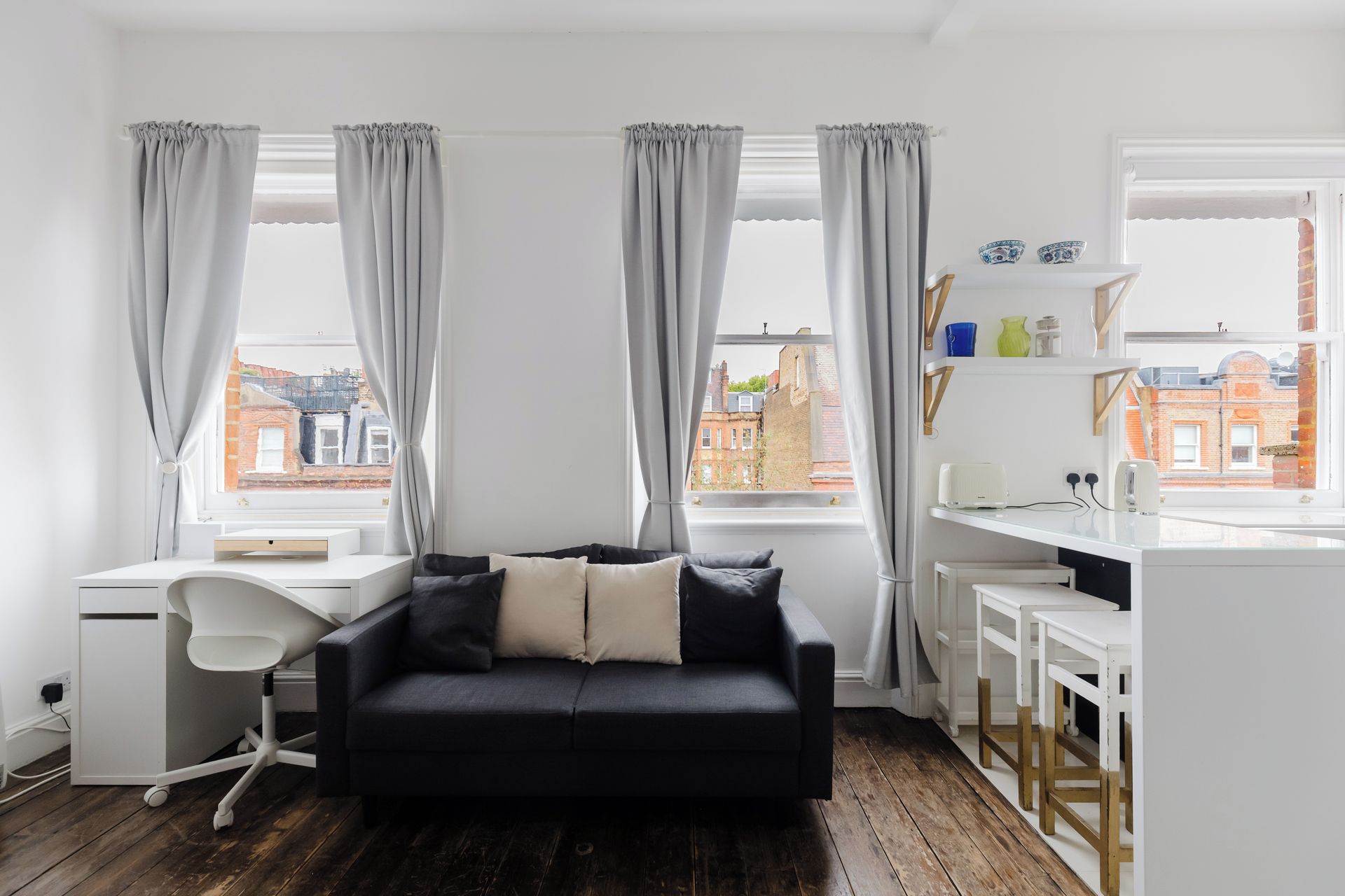 Een moderne kamer met een zwarte bank, een wit bureau en uitzicht op de stad.