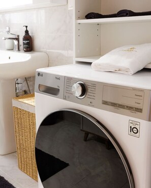 Een moderne wasruimte met een witte wasmachine, een rieten mand en een witte wasbak.