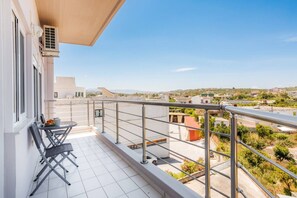 A balcony with a table and chairs, overlooking a residential area with buildings and greenery. - Plumeria Apartment Chania (Theriso)
