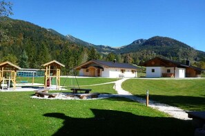 Eine Berghütte mit einem deutlichen Weg zum Eingang, umgeben von üppigem Grün und einem Bergpanorama.