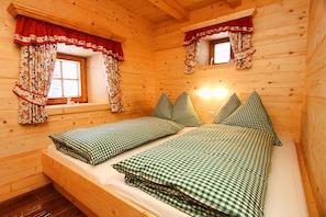 Ein Zimmer in einer Holzhütte mit zwei Betten, einem Fenster mit Vorhängen und einer geneigten Decke.