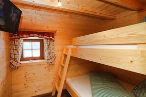 A wooden cabin room with bunk beds, a window with curtains, and a television mounted on the wall. - & Almhütte "Sonntagshorn" (Unken)