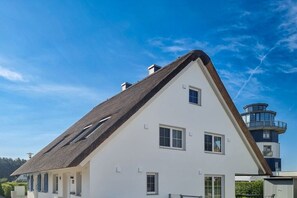 A white building with a steeply pitched roof, multiple windows, and a tower-like structure in the background. - Holiday home with 3 bedrooms (Breege\/ Juliusruh OT Breege)