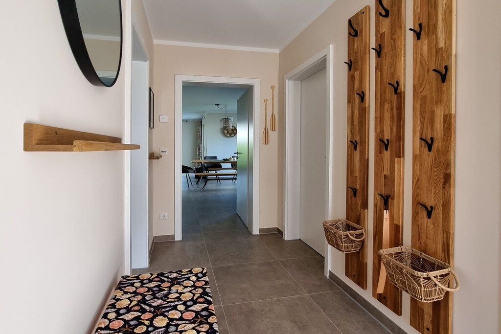 Un couloir avec un tapis à motifs, des crochets en bois fixés au mur et des paniers.