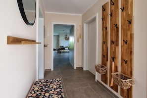 Um corredor com tapete estampado, ganchos de madeira fixados na parede e cestas.