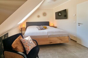 A bedroom with a sloped ceiling, a bed with a wooden frame, two bedside lamps, and a door. - Holiday home with 3 bedrooms (Breege\/ Juliusruh OT Breege)