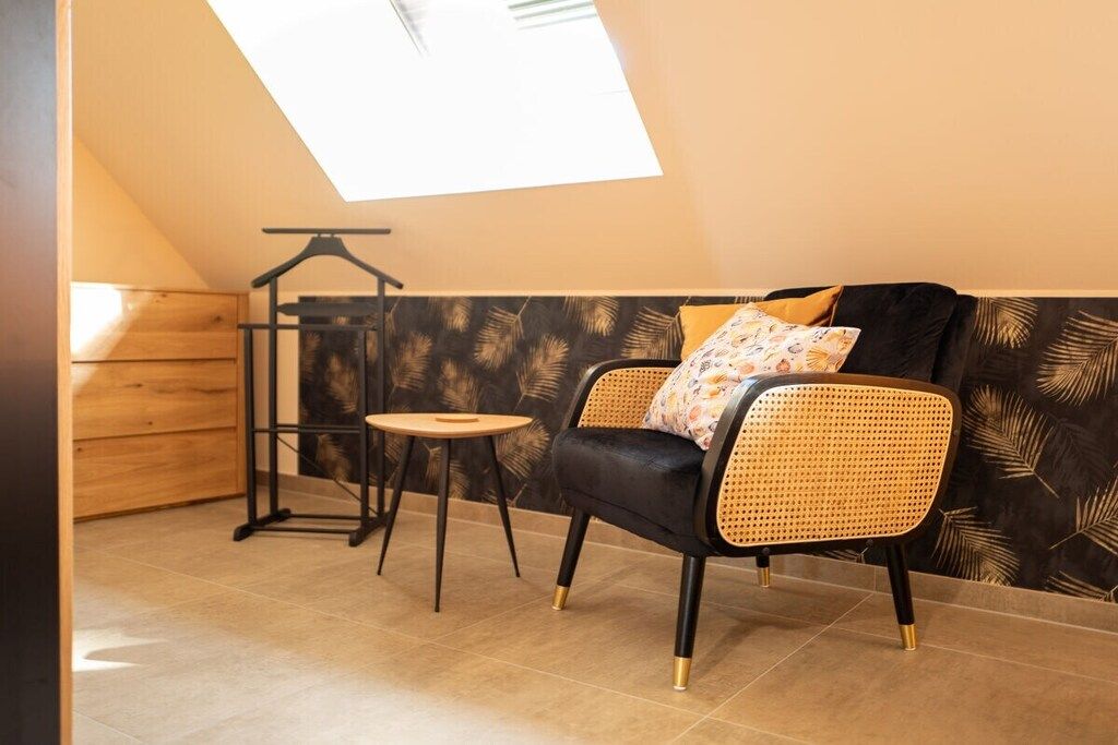 A room with a ceiling skylight, a black leather sofa with a woven backrest, a small round table, and a wooden wardrobe.