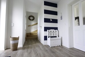 A hallway with a wooden staircase, a white bench, and a wicker basket. - Holiday home with 2 bedrooms (Fuhlendorf)