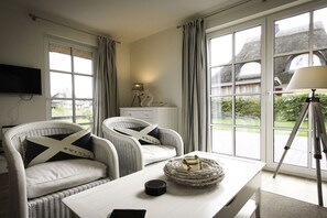 A room with two white armchairs, a white table, a lamp, and a tripod. - Holiday home with 2 bedrooms (Fuhlendorf)