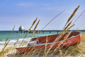 A beach scene with a red boat, a pier, and a domed structure in the background. - Holiday home with 2 bedrooms (Fuhlendorf)