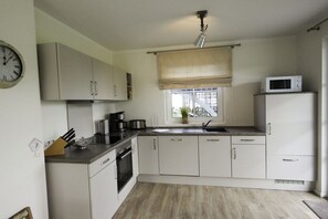 A compact kitchen with white cabinets, a microwave, a sink, and a clock on the wall. - Holiday home with 2 bedrooms (Fuhlendorf)