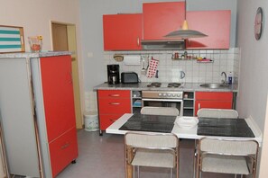 Una cuina compacta amb armaris vermells, una placa de cocció, un rentaplat i una taula de dinar amb caires.
