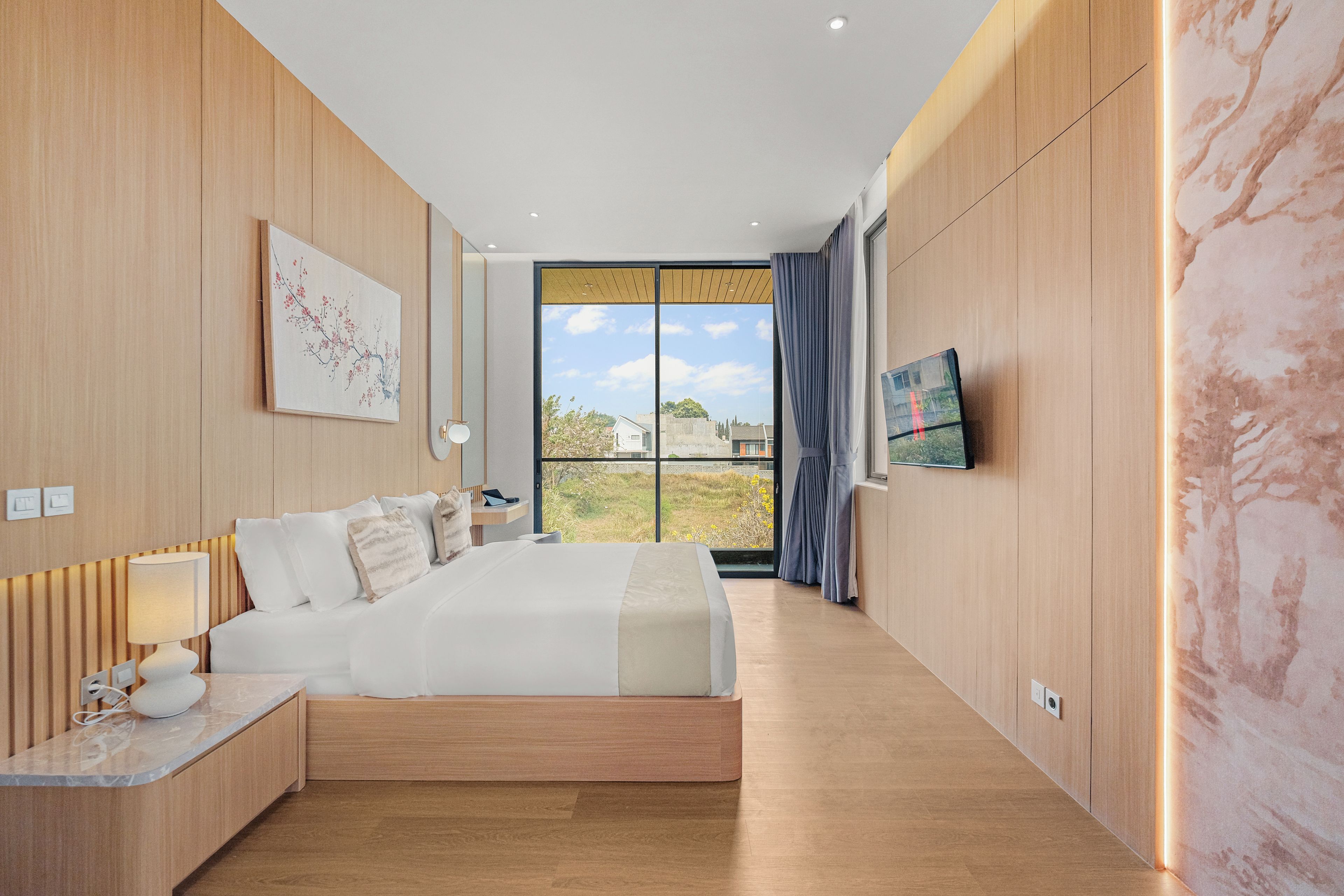 A modern hotel room with a large bed, a desk, and a TV on the wall.