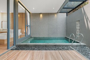 Una piscina interior moderna con pared de cristal, suelo de madera y borde de guijarros.